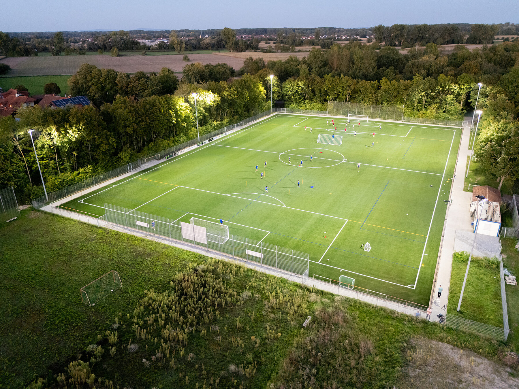 Beleuchteter Sportplatz aus der Luft in der Abenddämmerung, Training läuft