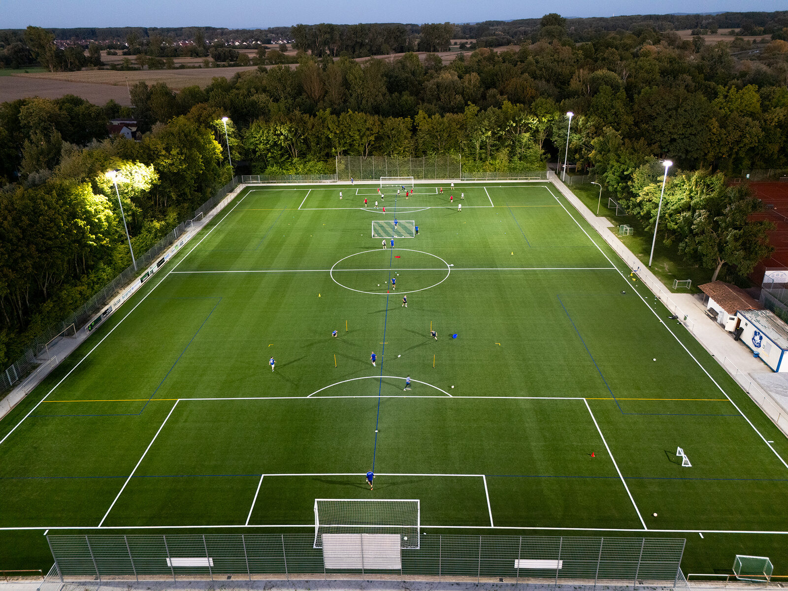 Beleuchteter Sportplatz aus der Luft, Blick über die ganze Länge des Platzes in der Dämmerung